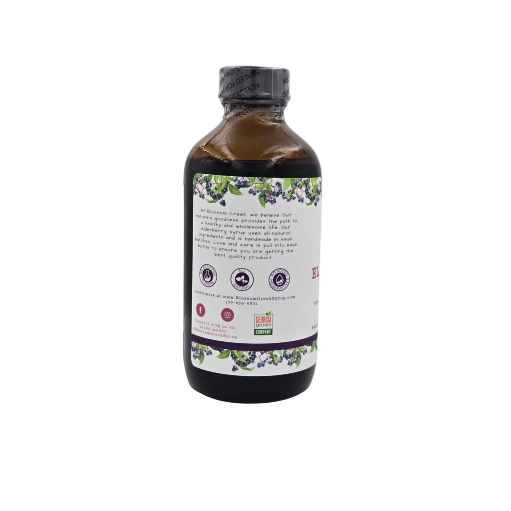 Side view of Blossom Creek 8 oz Elderberry Syrup in an amber glass bottle, featuring the white label with our company story, purple elderberry illustrations, and Georgia Grown logo.